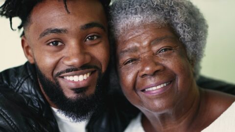 A smiling grandson embracing his elderly grandmother.
