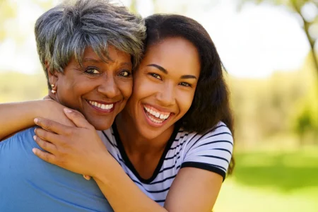 A joyful family caregiver embracing her smiling elderly mother outdoors in Georgia.